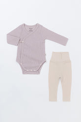 Avauma Selina Babysuit in a lavender haze color shown with matching beige baby leggings, highlighting the soft ribbed cotton and wrap-style closure for easy changing.